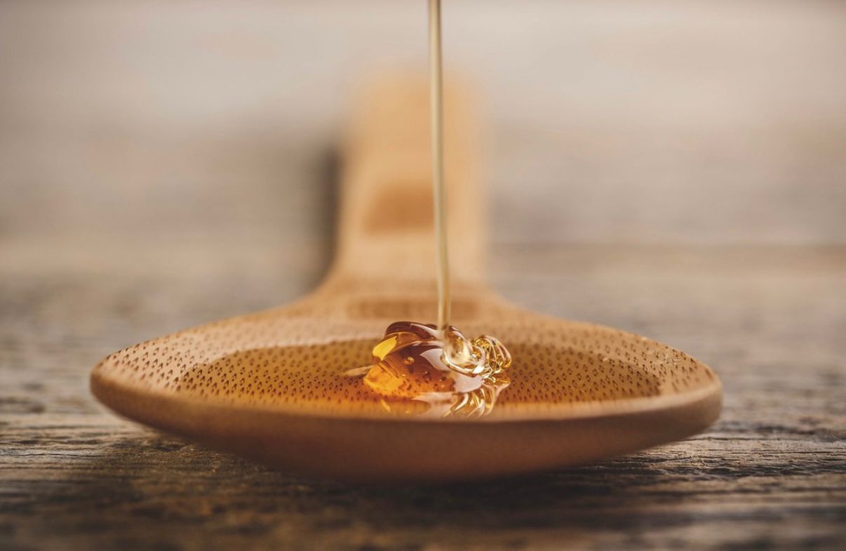 Honey being drizzled onto a wooden spoon with a blurred background